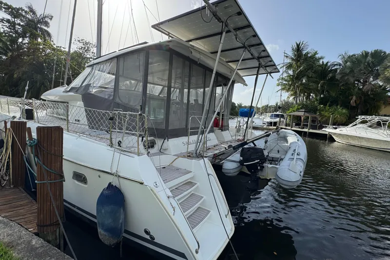 Slide: The Image of 2008 Lagoon 420 catamaran docked by a serene waterfront with lush greenery. - 1