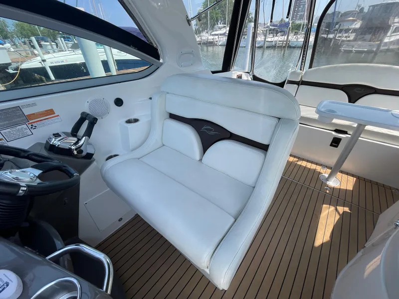Slide: The Image of 2013 Rinker 310 Express Cruiser cockpit with white seating and wood flooring, docked at marina. - 15