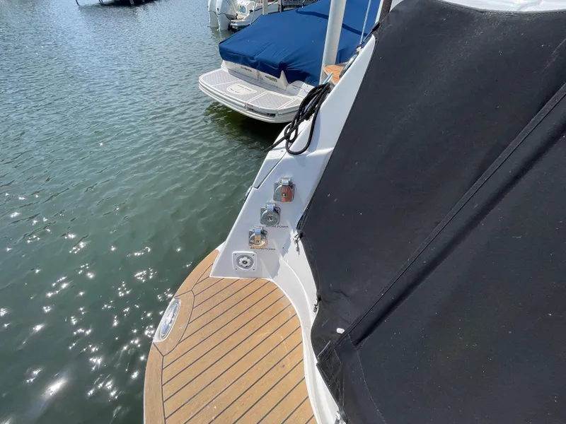 Slide: The Image of 2013 Rinker 310 Express Cruiser with wooden deck and black cover, docked on calm water. - 7