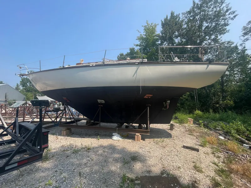 The Image of 1980 Cape Dory 36 sailboat on dry dock, surrounded by trees and gravel. - 1