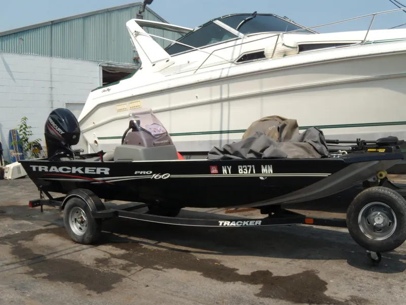 Slide: The Image of 2018 Tracker Pro 160 boat on trailer, parked beside a larger yacht. - 2