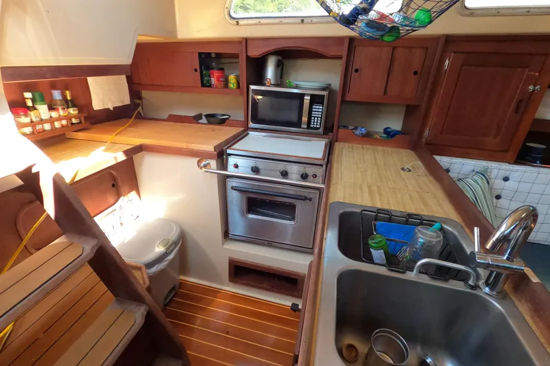Slide: The Image of 1983 Catalina 36 yacht kitchen with stove, microwave, sink, and wooden cabinetry. - 17