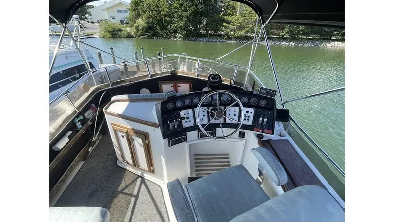Slide: The Image of 1986 Carver 3607 Aft Cabin helm with steering wheel and control panel, docked by a river. - 3