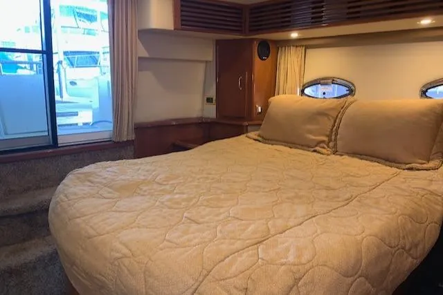 Slide: The Image of 2005 Carver 444 Cockpit Motor Yacht bedroom with cozy bedding and porthole windows. - 27