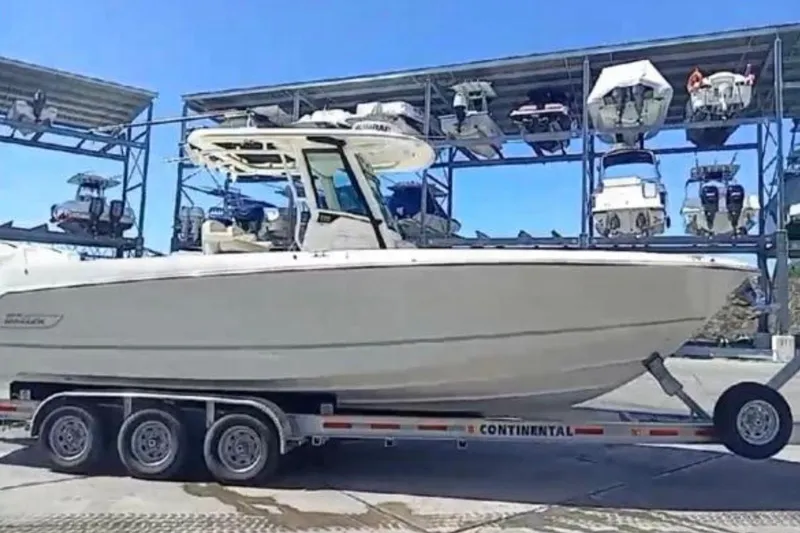 Slide: The Image of 2024 Boston Whaler 280 Outrage on trailer, parked in marina with boats in background. - 0