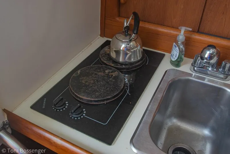 Slide: The Image of 1999 Mainship Pilot 30 galley with stove, kettle, sink, and soap dispenser. - 16