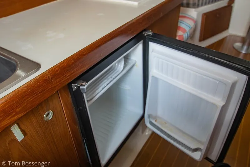 Slide: The Image of 1999 Mainship Pilot 30 interior with open mini fridge and wooden countertop. - 18