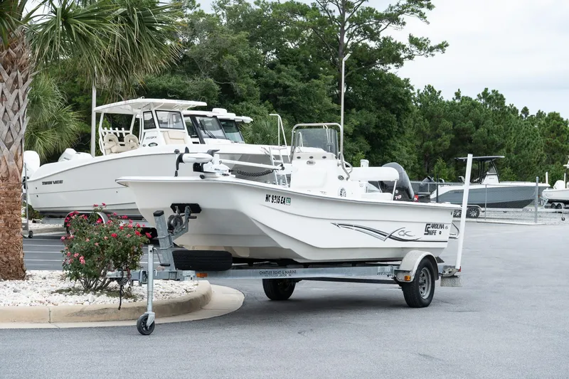 Slide: The Image of 2015 Carolina Skiff 1980 DLX boat on trailer, parked near palm tree and other boats. - 2