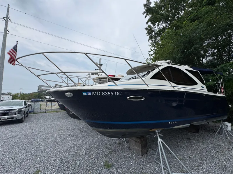 The Image of 2016 Cutwater C-24 boat on stands, gravel lot, American flag, overcast sky. - 1