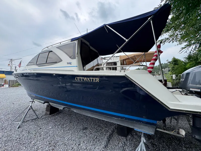 Slide: The Image of 2016 Cutwater C-24 boat with blue hull and canopy, displayed on gravel. - 2