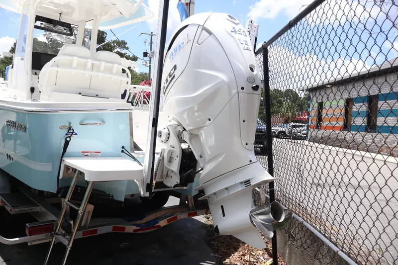 Slide: The Image of 2025 Regulator 26XO boat with Yamaha outboard motor, parked near a chain-link fence. - 2