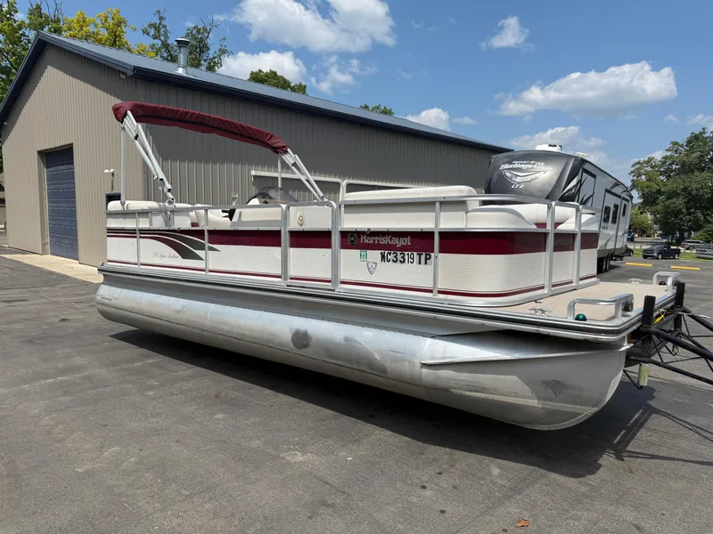 Slide: The Image of 2000 Harris 200 Super Sunliner pontoon boat parked near a garage under a clear sky. - 1