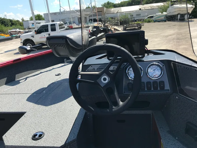 Slide: The Image of 2026 Lund 1800 Explorer SS boat with seating and motor, parked near industrial silos. - 9