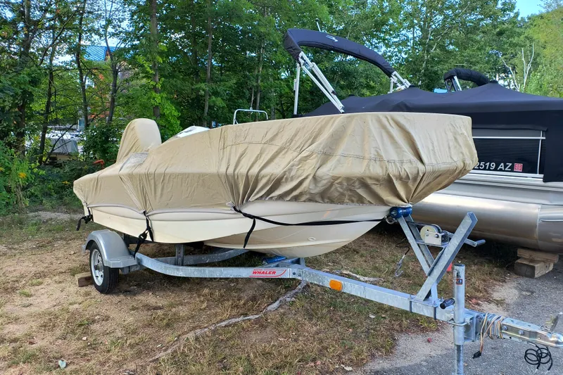 Slide: The Image of 2016 Boston Whaler 130 Super Sport boat covered on a trailer, parked outdoors. - 9