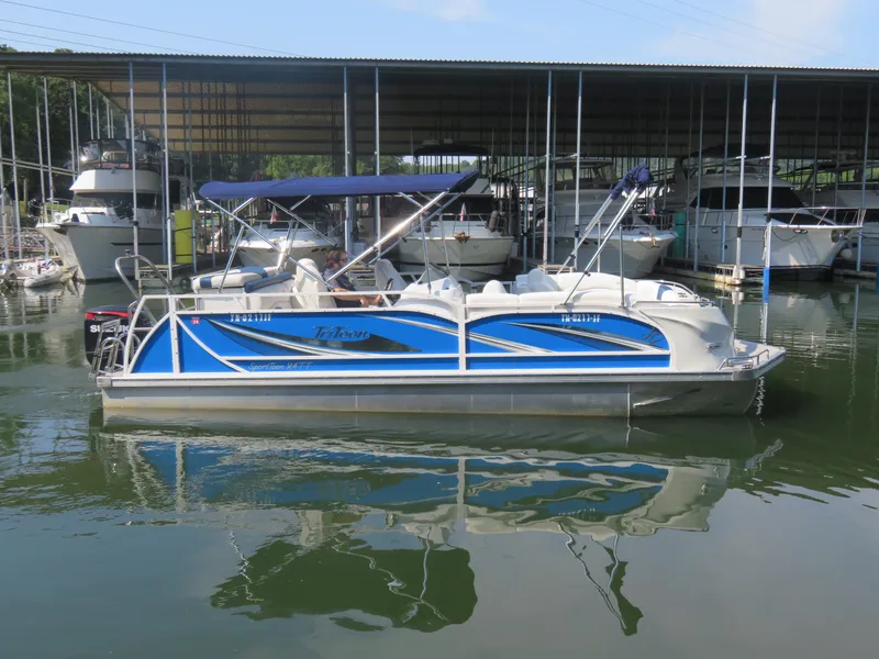 The Image of 2021 JC SportToon 24 TT CS pontoon boat docked in marina, blue and white design. - 0