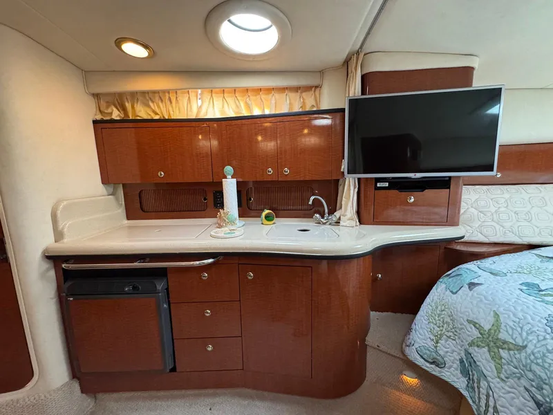 Slide: The Image of Interior of 2003 Sea Ray 320 Sundancer with kitchenette and TV, featuring wood cabinetry. - 14