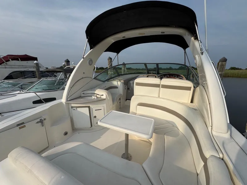 Slide: The Image of 2003 Sea Ray 320 Sundancer boat interior with white seating and table, docked by the water. - 3