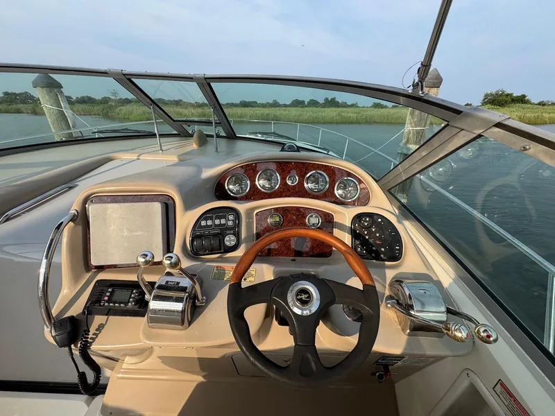 Slide: The Image of 2003 Sea Ray 320 Sundancer helm with wood accents and modern controls, docked by calm waters. - 6
