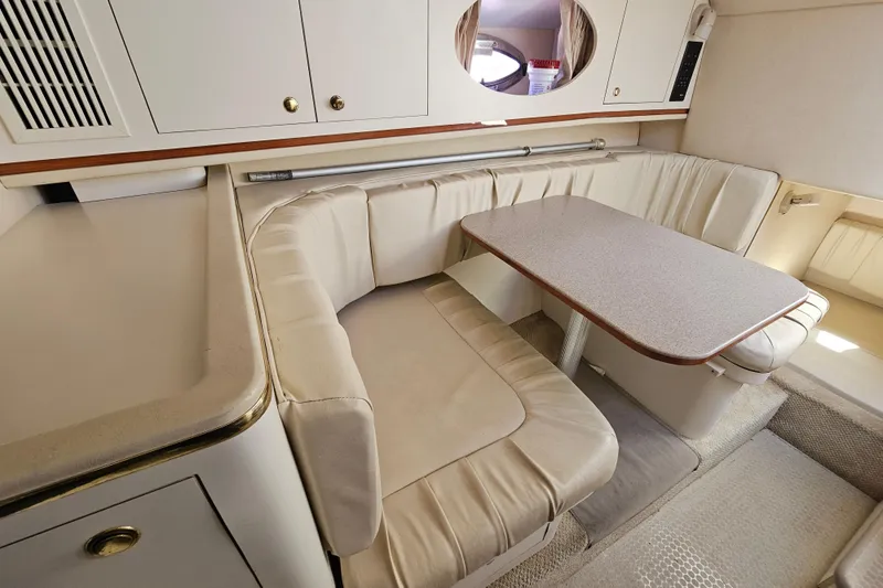Slide: The Image of 2001 Sea Ray 290 Amberjack cabin with beige seating and table, featuring storage cabinets. - 23