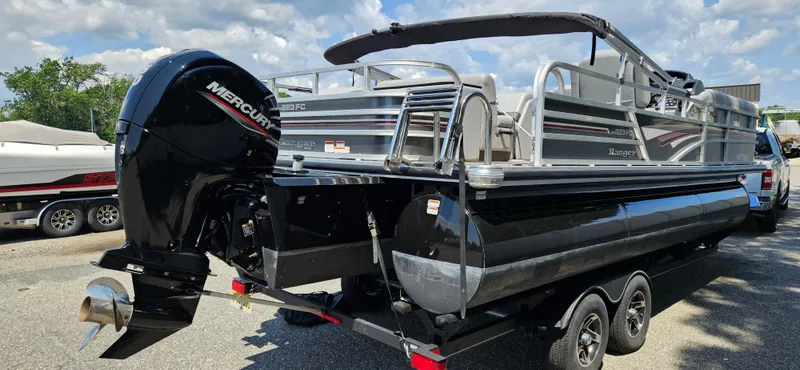 Slide: The Image of 2022 Ranger 223FC pontoon boat with Mercury outboard motor on a trailer, parked outdoors. - 4