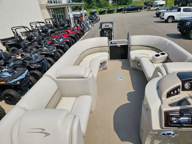 Slide: The Image of 2014 Bennington 2275 GL pontoon boat interior with beige seating, parked near ATVs and vehicles. - 18