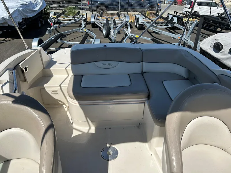 Slide: The Image of 2004 Sea Ray 220 Sundeck interior with beige seating and boat trailers in the background. - 16