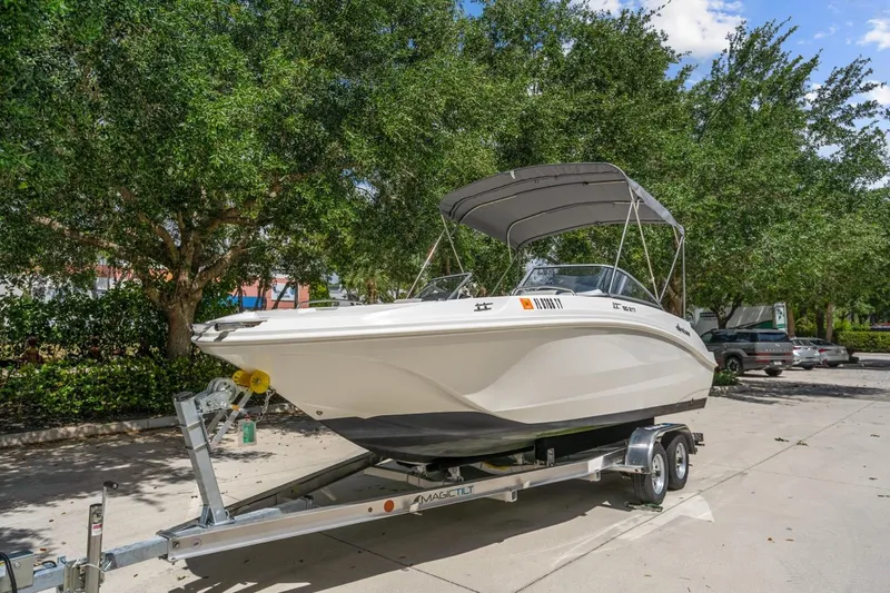 Slide: The Image of 2025 Hurricane SunDeck 217 OB boat on trailer, parked outdoors with trees in background. - 5