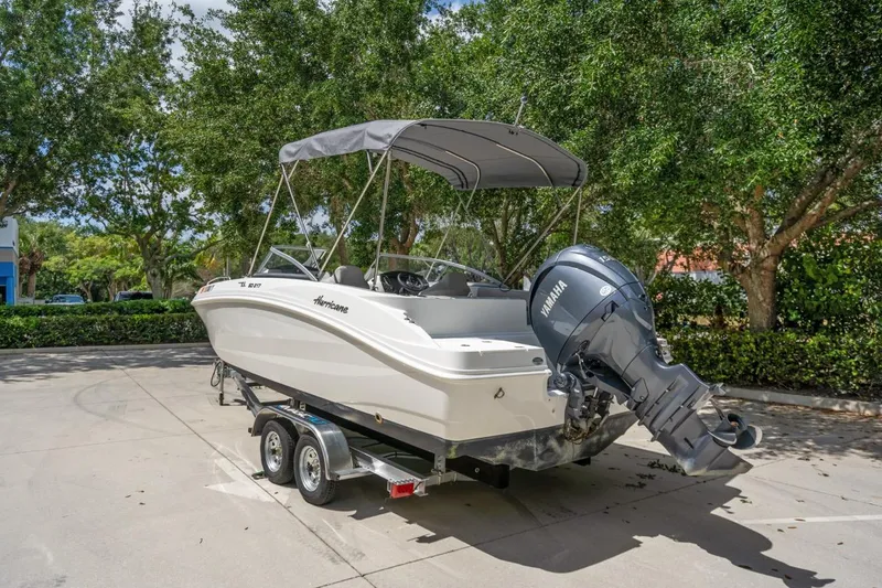 Slide: The Image of 2025 Hurricane SunDeck 217 OB boat on trailer, parked outdoors with trees in background. - 6