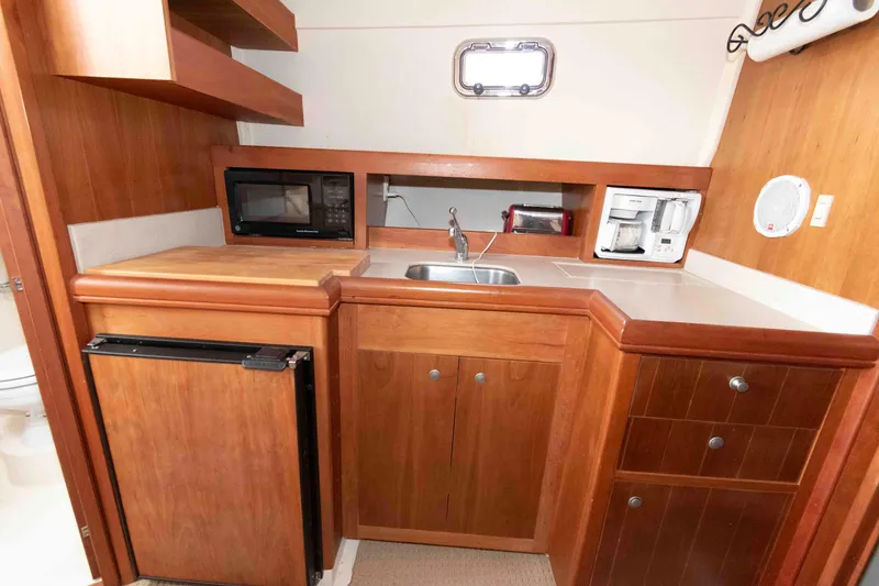 Slide: The Image of 2004 Mainship 34 Pilot Rum Runner II galley with wood cabinetry, sink, microwave, and coffee maker. - 11