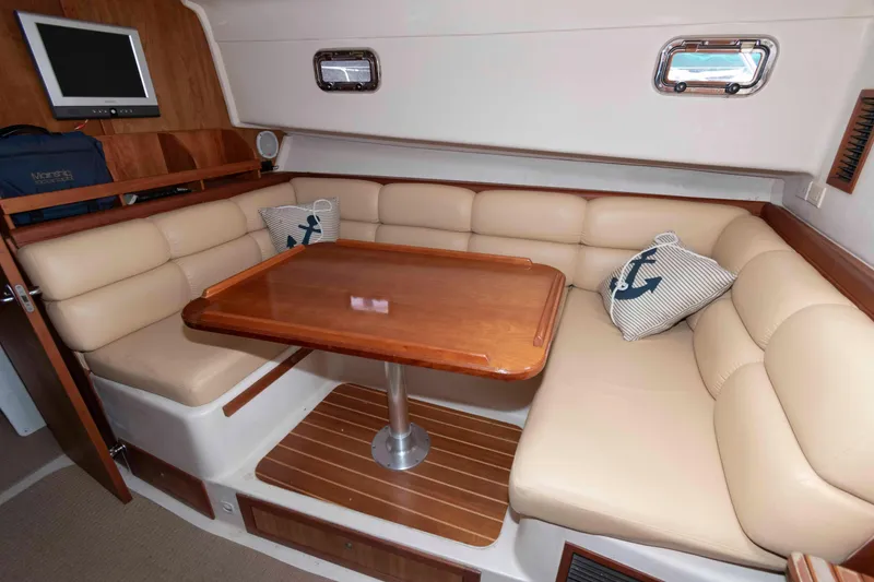 Slide: The Image of 2004 Mainship 34 Pilot Rum Runner II interior with beige seating and wooden table. - 12