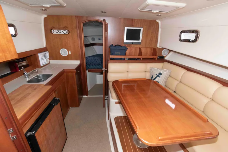Slide: The Image of 2004 Mainship 34 Pilot Rum Runner II interior with kitchenette, dining area, and cozy seating. - 14