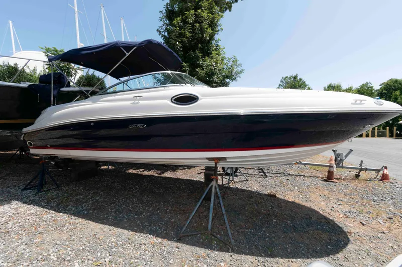 The Image of 2006 Sea Ray 240 Sundeck boat on stands, outdoors, with blue canopy. - 0