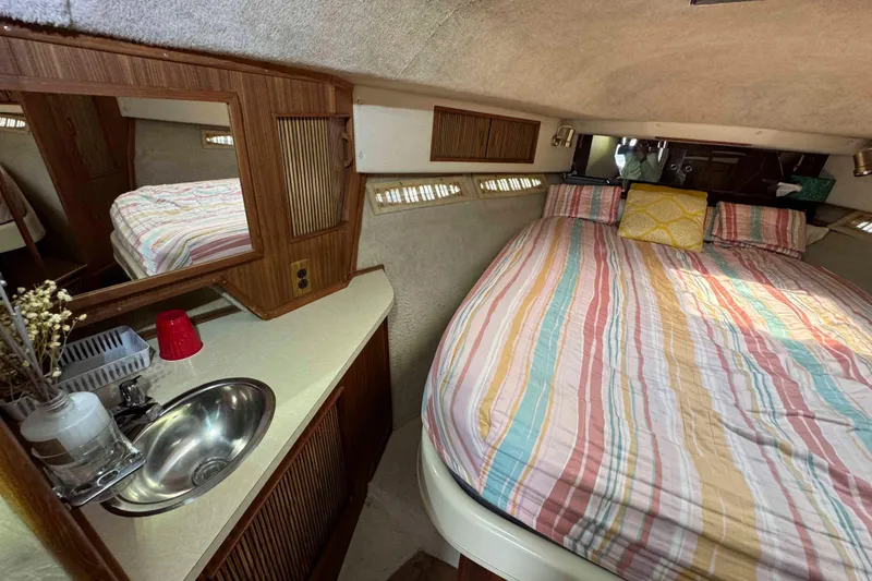 Slide: The Image of 1986 Sea Ray 390 Express Cruiser cabin with striped bedding and compact sink area. - 15