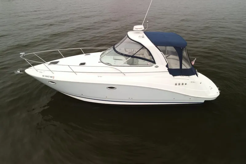 The Image of 2009 Rinker 340 Express Cruiser on calm water, featuring sleek white design and blue canopy. - 0