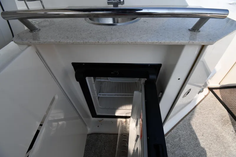 Slide: The Image of 2011 Sea Ray 310 Sundancer boat kitchenette with open mini fridge and countertop sink. - 25