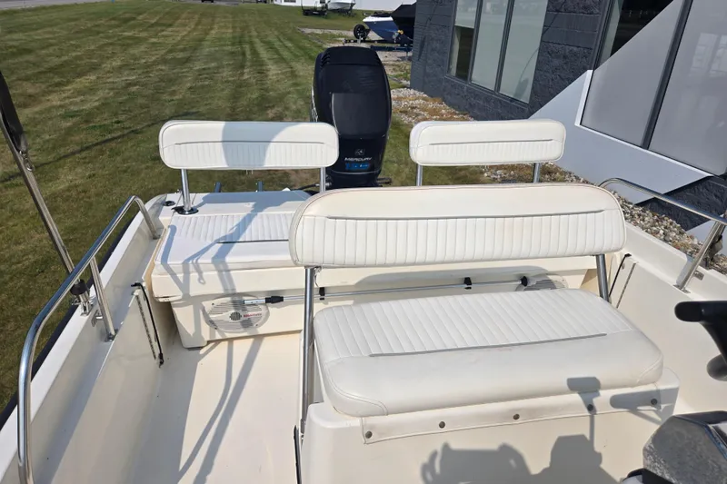 Slide: The Image of 1998 Boston Whaler 18 Dauntless boat interior with white seating and motor, parked on grass. - 11