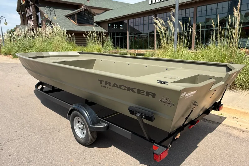 Slide: The Image of 2026 Tracker Grizzly 2072 Utility boat on trailer, parked outside a rustic building. - 3