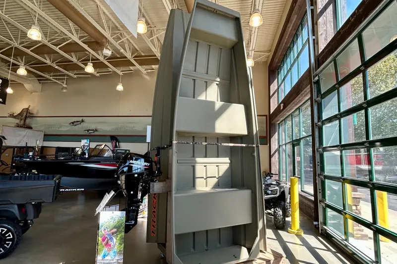 Slide: The Image of 2026 Tracker Grizzly 14 Jon boat displayed in a showroom with high ceilings. - 2