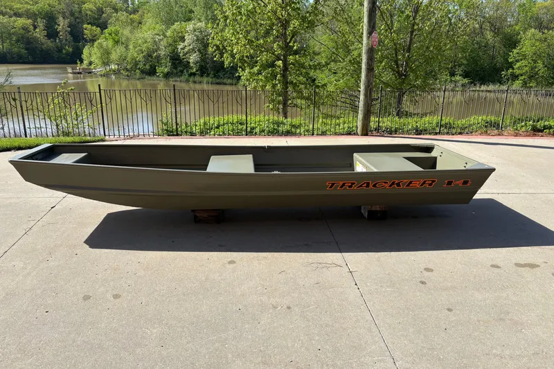The Image of 2026 Tracker Grizzly 14 Jon boat on concrete near a scenic lake. - 0