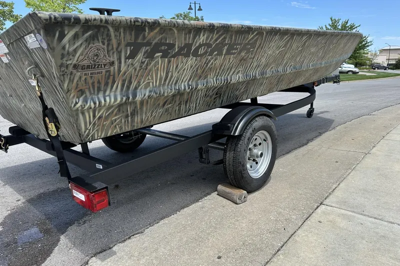 Slide: The Image of 2026 Tracker Grizzly 1648 Utility boat on trailer, featuring camo design, parked on street. - 4