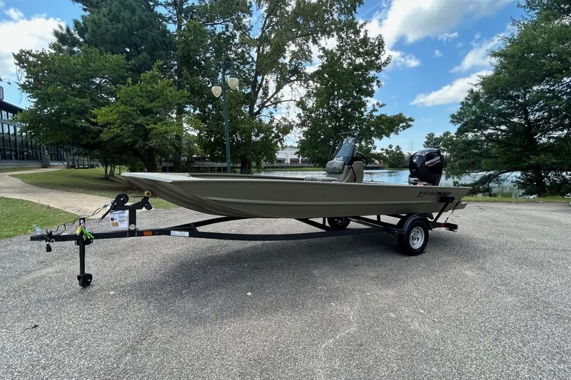 Slide: The Image of 2026 Tracker Grizzly 1860 CC boat on trailer, parked near a lake with trees. - 60