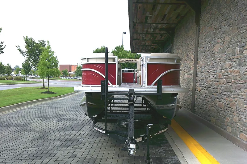 Slide: The Image of 2025 Sun Tracker Party Barge 24 DLX pontoon boat on trailer, parked near stone wall. - 2