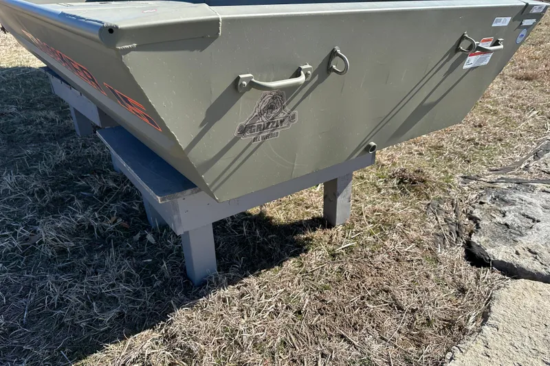 Slide: The Image of 2026 Tracker Grizzly 15 Jon boat on display, resting on a wooden stand outdoors. - 11
