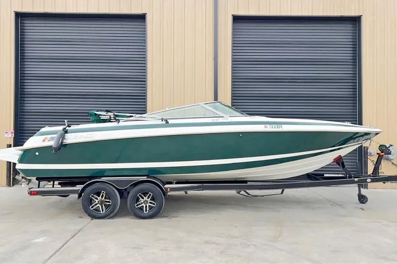 The Image of 2000 Cobalt 252 boat on trailer, green and white, parked outside industrial building. - 0