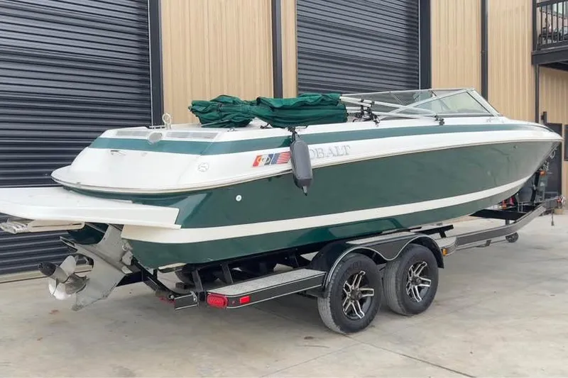 Slide: The Image of 2000 Cobalt 252 boat on trailer, green and white, parked near garage. - 2