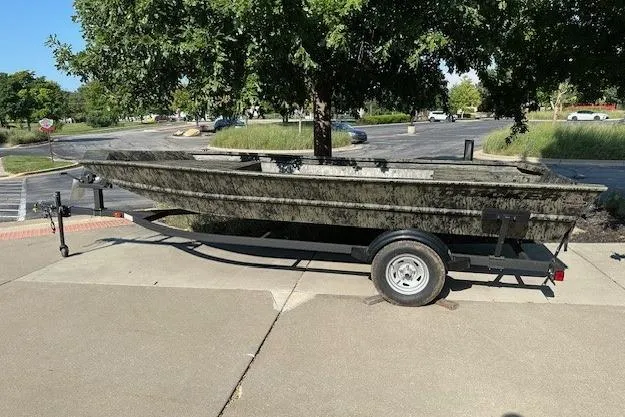 The Image of 2026 Tracker Grizzly 1754 Utility boat on trailer, parked outdoors under trees. - 0