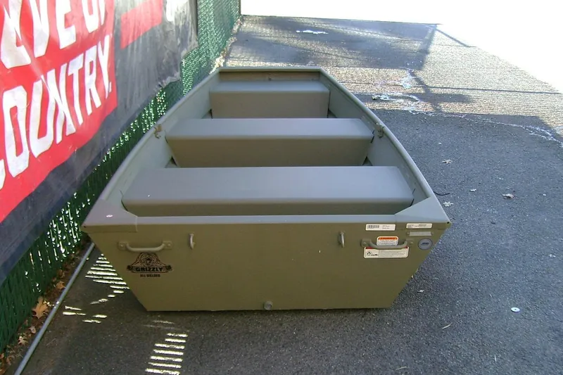 Slide: The Image of 2026 Tracker Grizzly 10 Jon boat, olive green, parked on pavement near a fence. - 5
