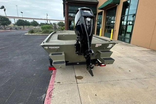Slide: The Image of 2026 Tracker Grizzly 1654 T Sportsman boat with outboard motor, parked outside a building. - 2