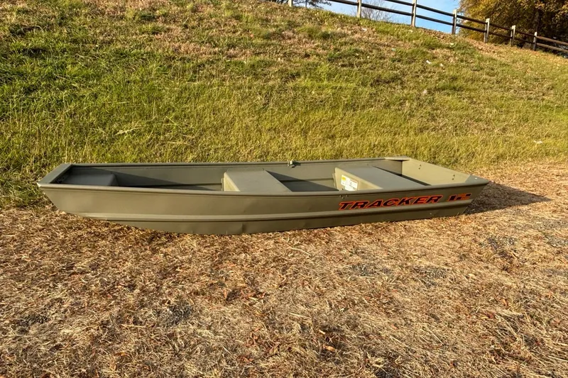 Slide: The Image of 2026 Tracker Grizzly 12 Jon boat on grassy terrain, side view. - 2