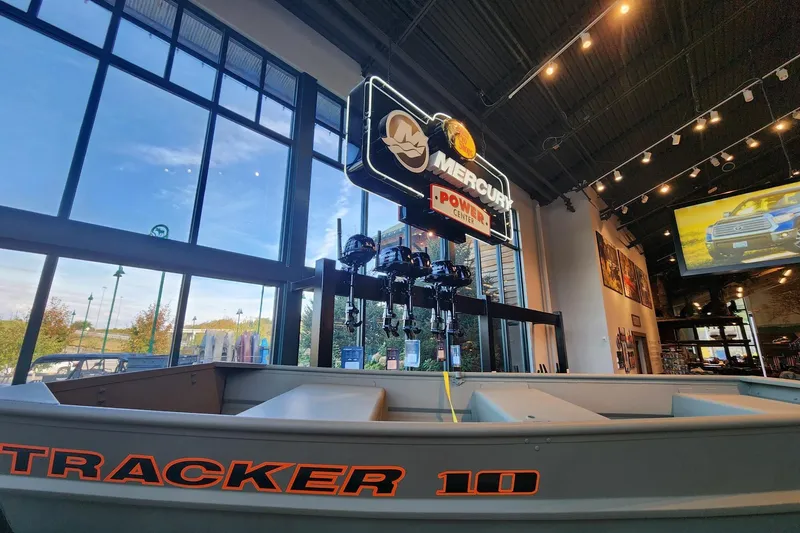 The Image of 2026 Tracker Grizzly 10 Jon boat displayed indoors with Mercury Power Center sign. - 0
